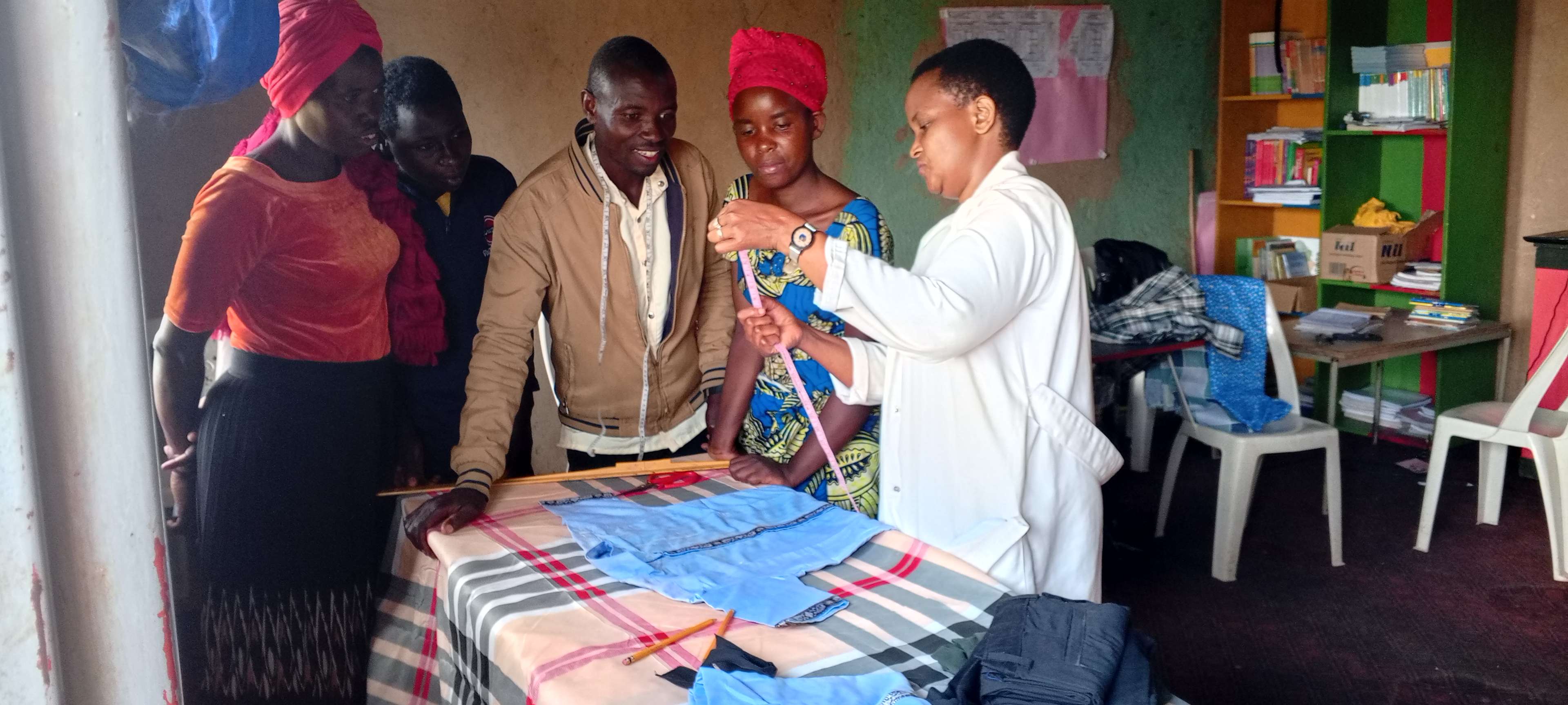 The trainees are being shown two parts of the measuring table as they learn out tailoring